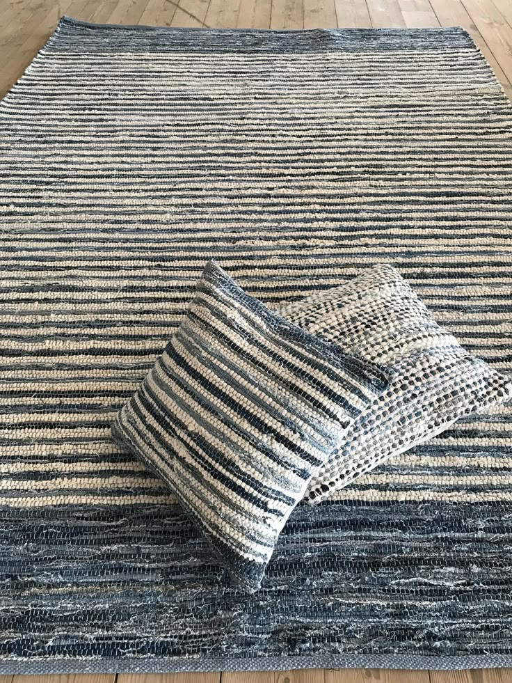 a blue and white striped rug with two pillows on the floor next to each other