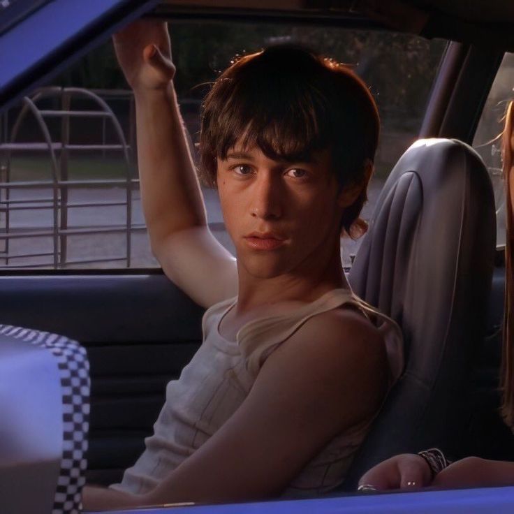 two young people sitting in the back seat of a car, one holding up his hand