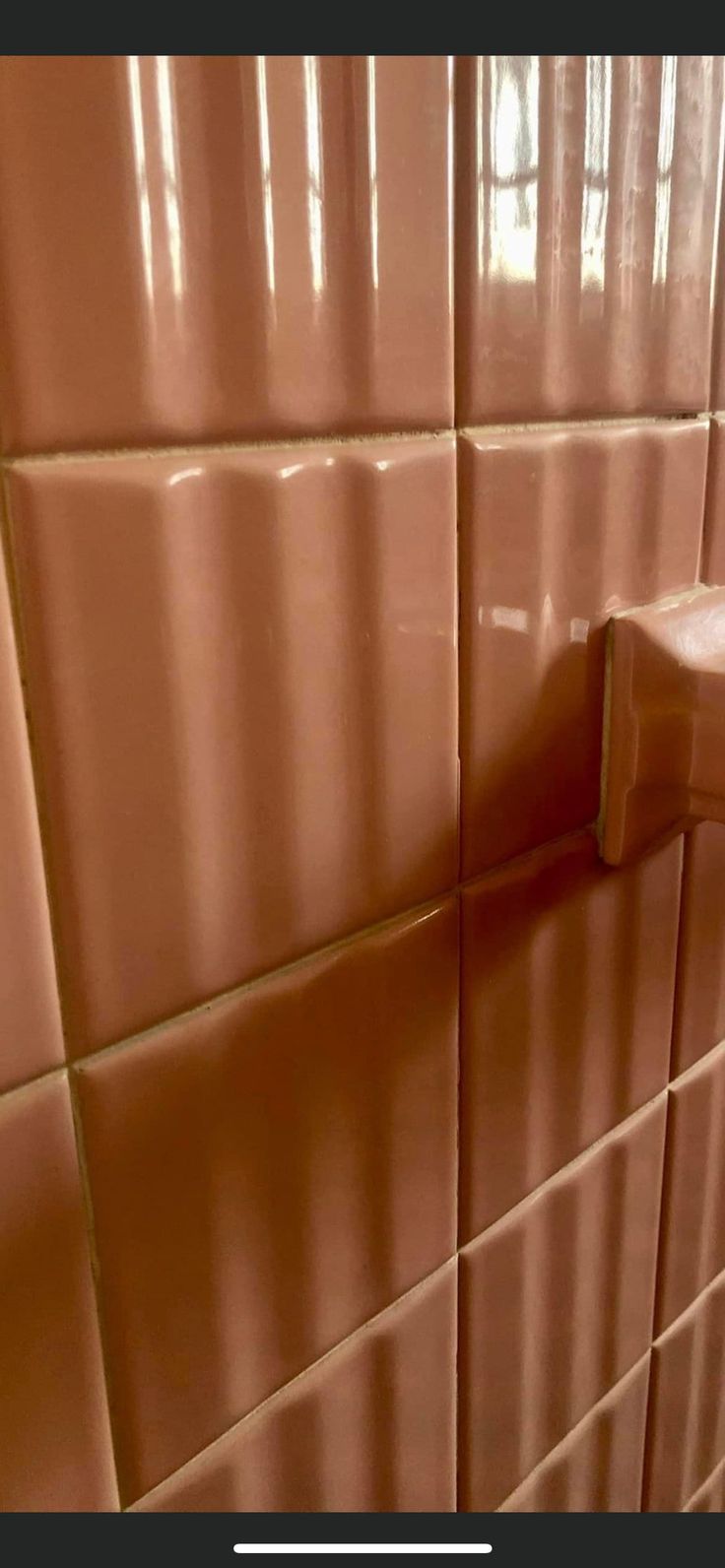 the corner of a bathroom with brown tiles and a white toilet paper dispenser