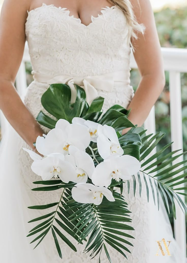 a woman in a wedding dress holding a bouquet of white flowers and greenery on the balcony