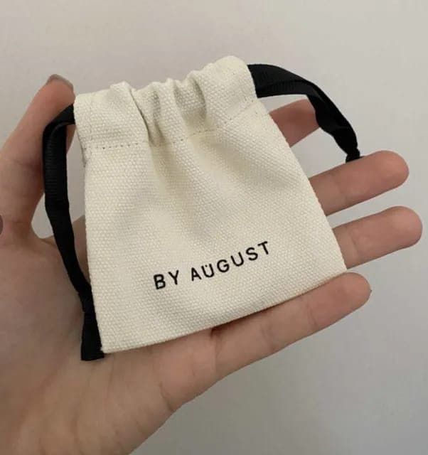 a hand holding a small bag with the word by august printed on it in black ink