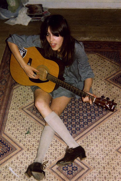 a woman sitting on the floor with a guitar in her hand and wearing knee high socks