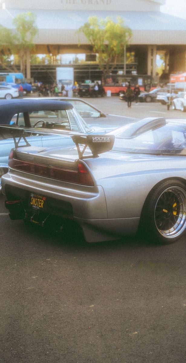 a silver sports car parked in front of a parking lot with other cars behind it