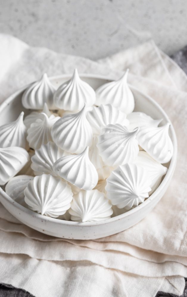 a white bowl filled with small shells on top of a cloth covered table next to a napkin