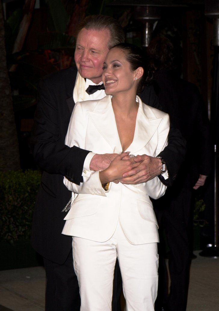 a man in a tuxedo hugging a woman who is wearing a white suit