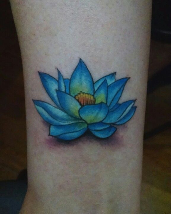 a blue lotus flower tattoo on the ankle with yellow center and green center, sitting on a woman's right leg