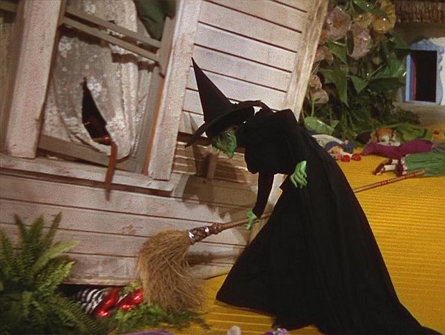 a woman dressed as a witch walking past a house with lots of decorations on it