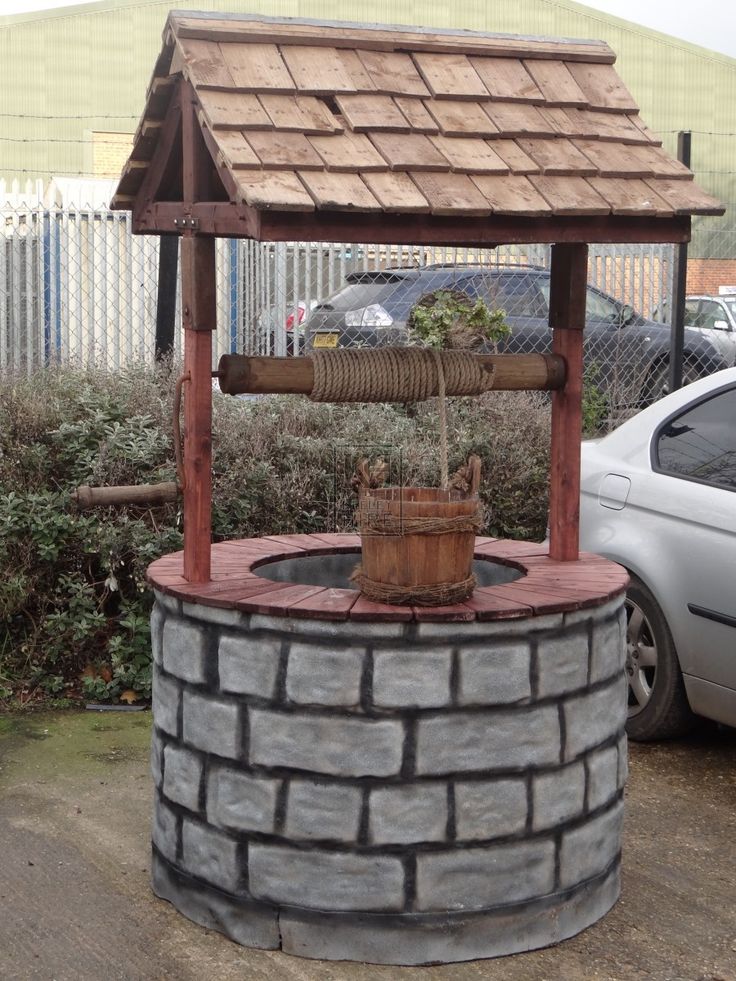 an outdoor water fountain made out of bricks with a wooden roof and bucket on top