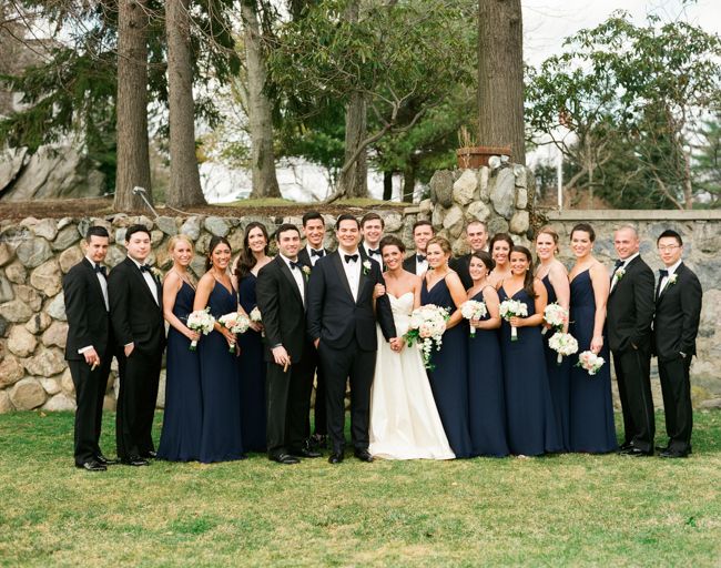 a group of people standing next to each other in front of a stone wall and trees