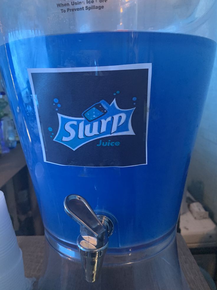 a blue soda machine sitting on top of a counter next to a plastic cup filled with water