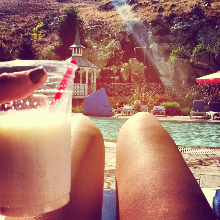 a person sitting next to a swimming pool with a drink in front of them on their lap