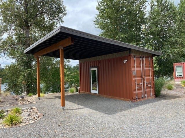 a small building made out of shipping containers in the middle of a gravel lot next to trees