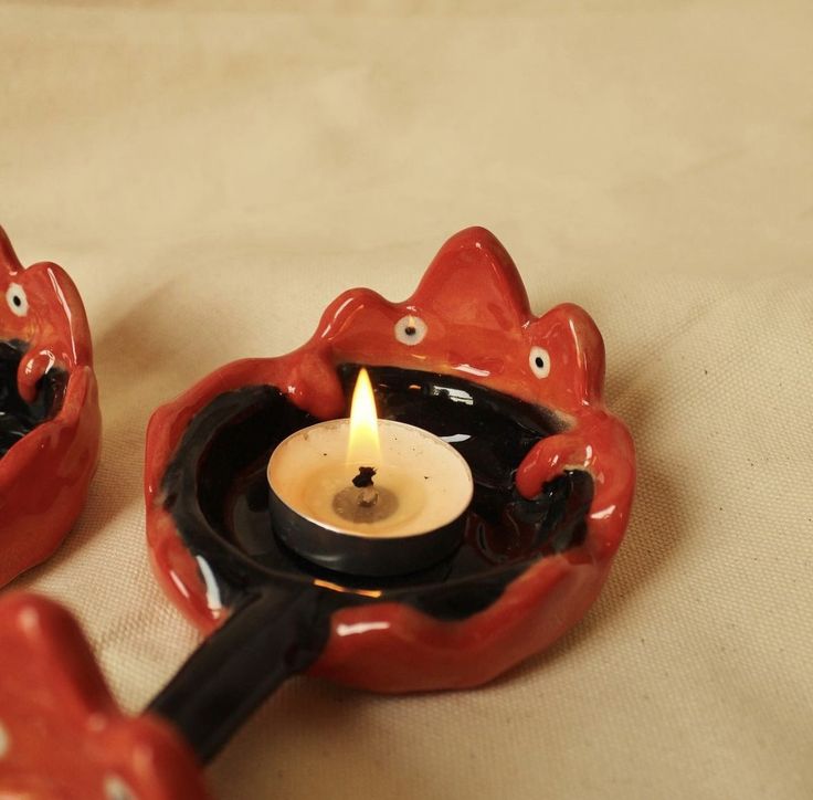 two red ceramic objects with a lit candle in the shape of cats sitting on top of each other