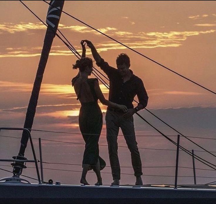 two people standing on the top of a boat at sunset with their arms in the air