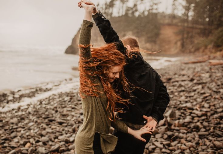 a man and woman are dancing on the rocks by the water with their arms in the air