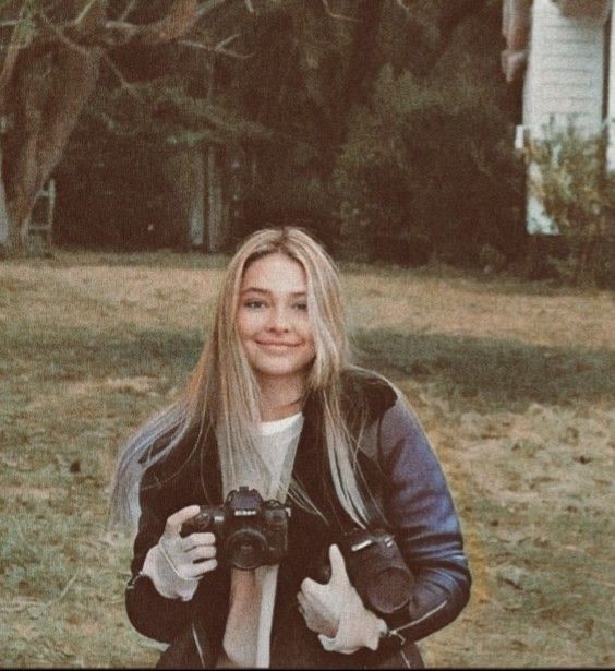 a woman taking a selfie with her camera in front of a house and trees