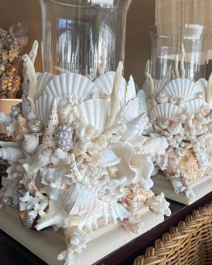 two vases with shells and seashells in them sitting on a table next to a wicker basket