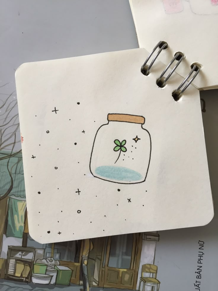 an open notebook with a drawing of a glass jar on it and a clover in the bottom