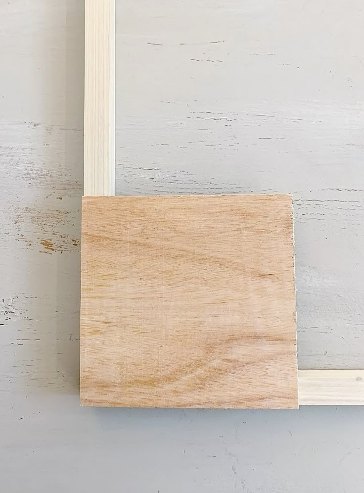 an unfinished piece of wood hanging on a white wall with a wooden frame attached to it