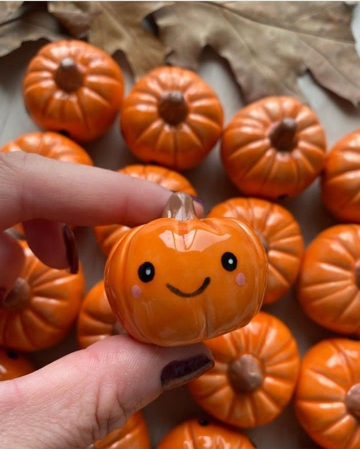 a hand holding an orange pumpkin with a smiley face on it's nose and surrounded by other small pumpkins