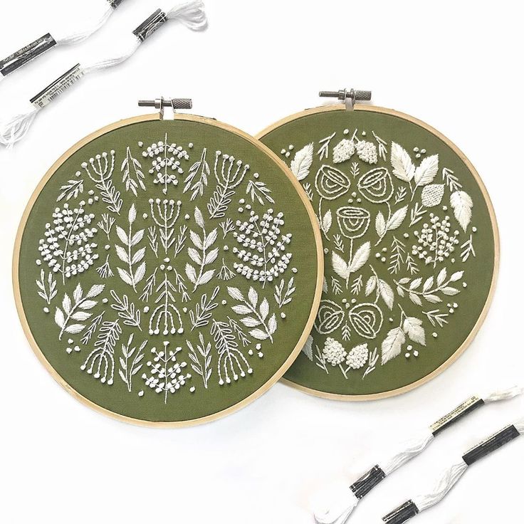 two green embroidered hoops with white flowers and leaves on them next to some wires