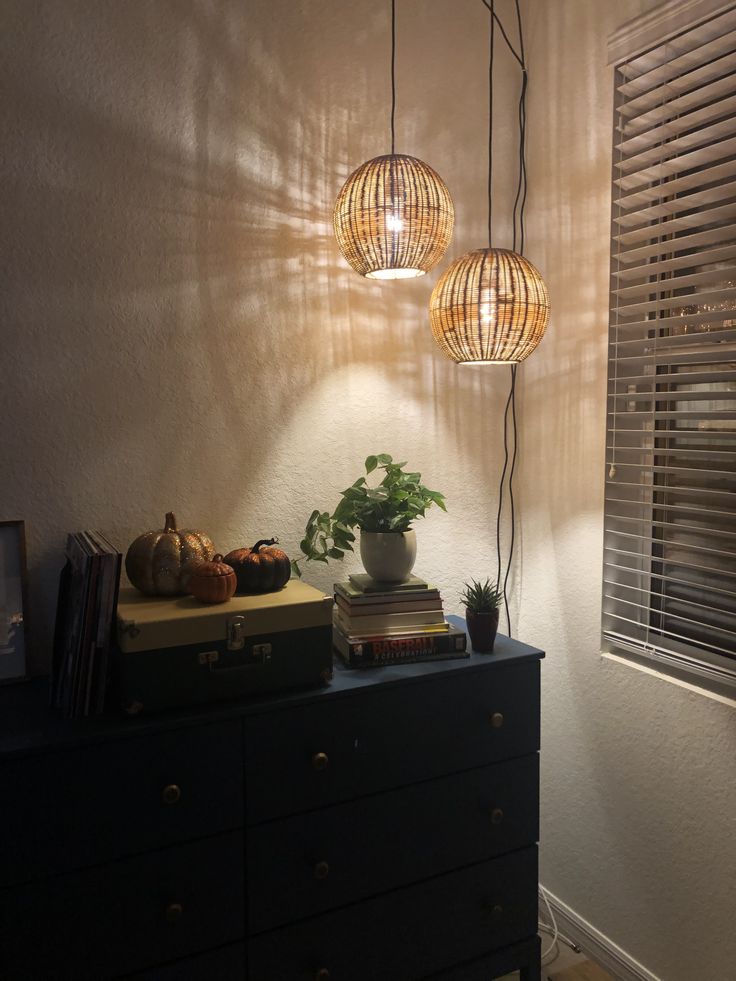 three lights hanging over a dresser next to a window with blinds on the windowsill