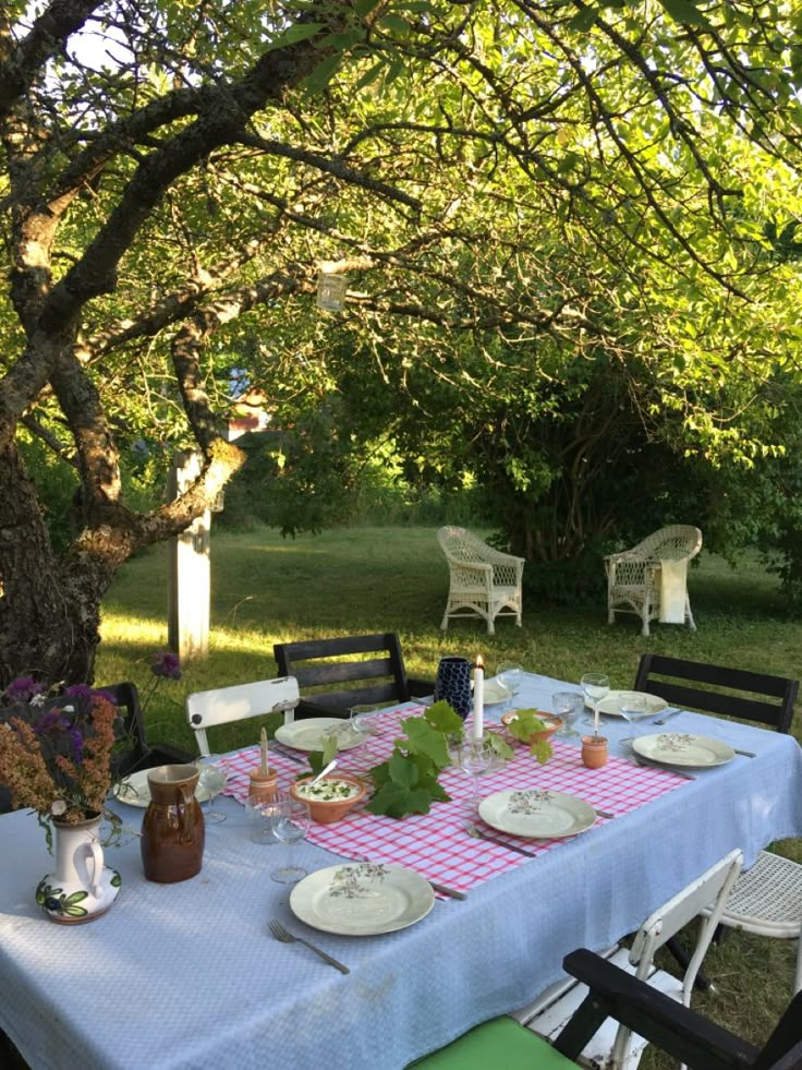 the table is set for two outside in the yard with flowers and plates on it