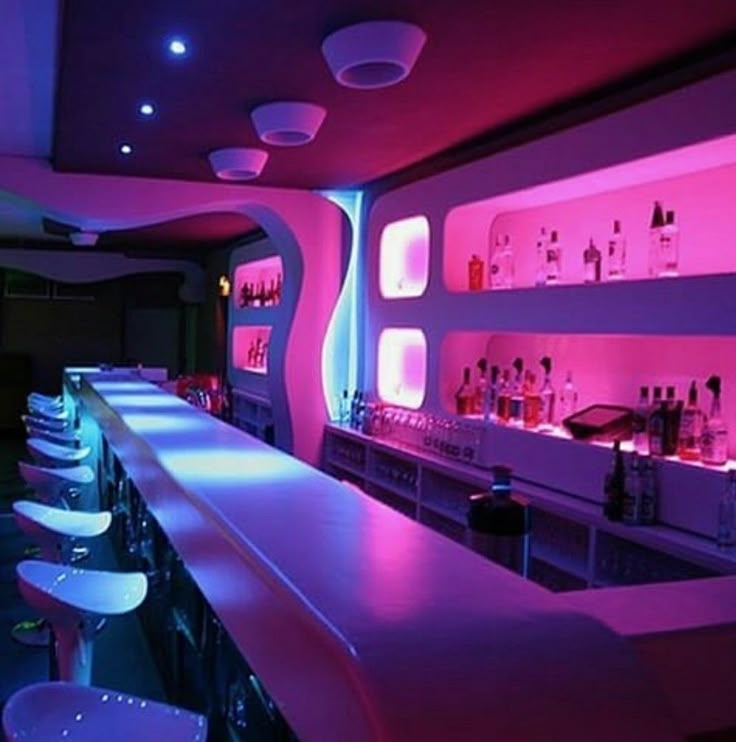 a dimly lit bar with white stools and neon lights on the wall behind it