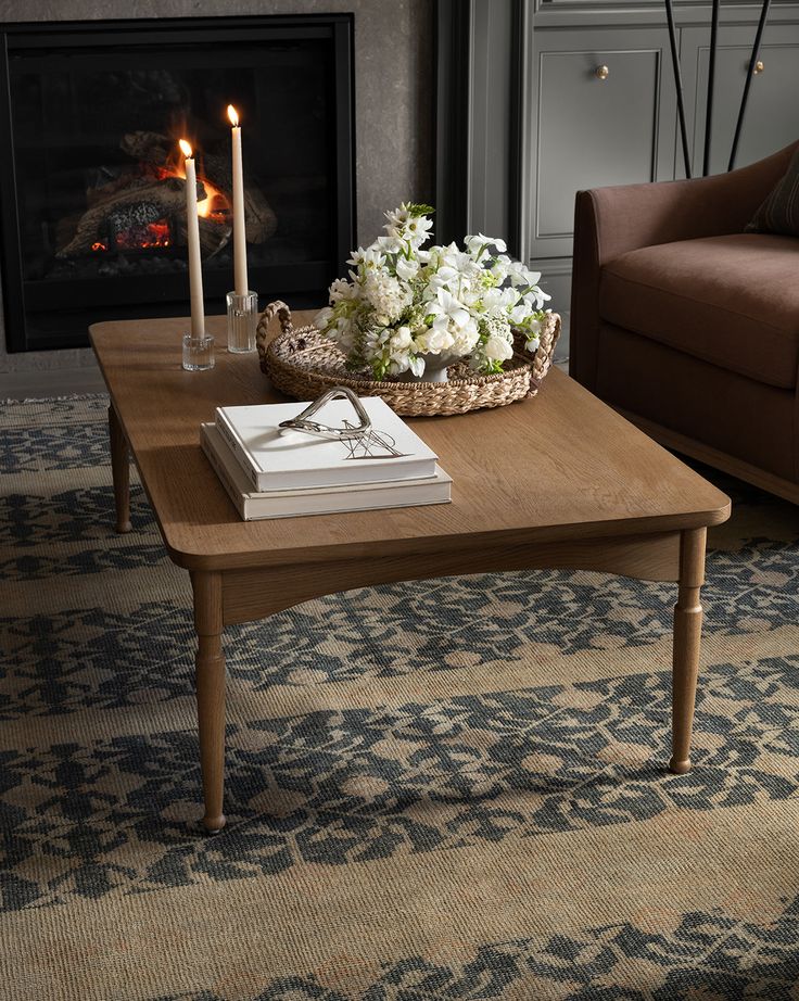 a coffee table with flowers and candles on it in front of a fire place, next to a couch