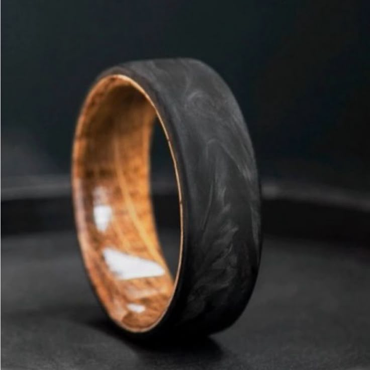 a wooden ring with black and gold inlays sits on a round metal surface