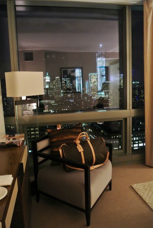 a hotel room with a view of the city lights and skyscrapers in the distance