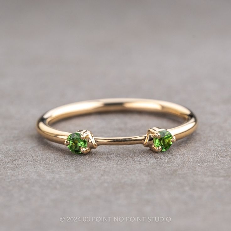 a gold ring with two green stones on the top and bottom, sitting on a gray surface