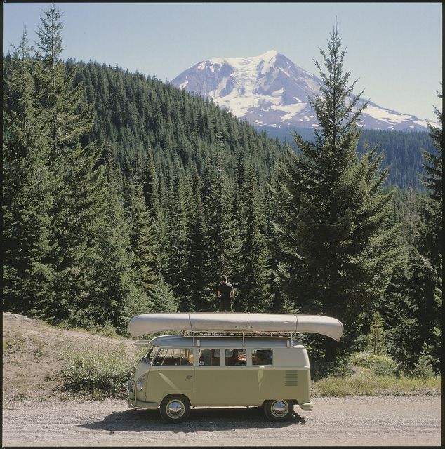 an old vw bus with a surfboard on the roof parked in front of trees