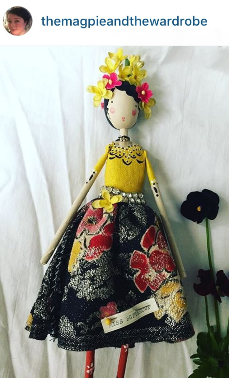 the doll is wearing a yellow top and black skirt with flowers on it's head