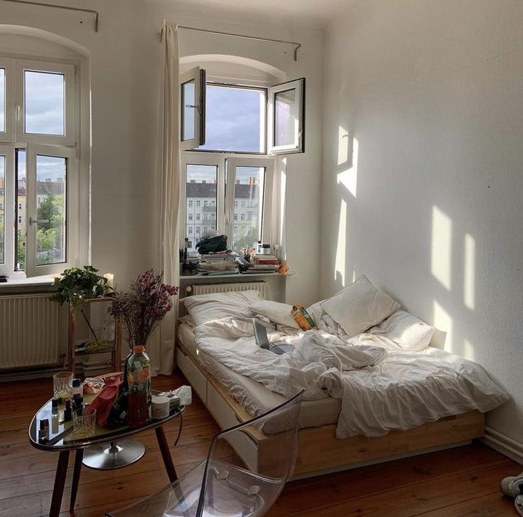 a bed sitting in the middle of a living room next to two windows with lots of sunlight coming through them