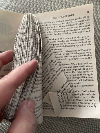 someone is holding an open book with paper folded over it and reading the same book