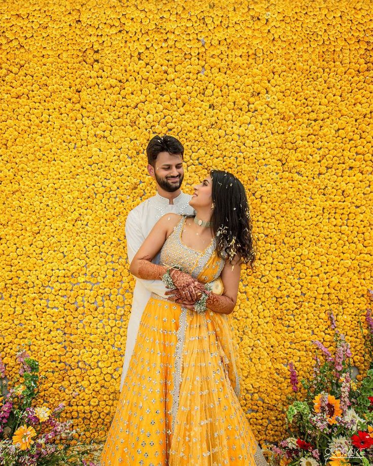 a man and woman standing next to each other in front of a yellow flower wall