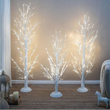 three white lighted trees in front of a gray wall