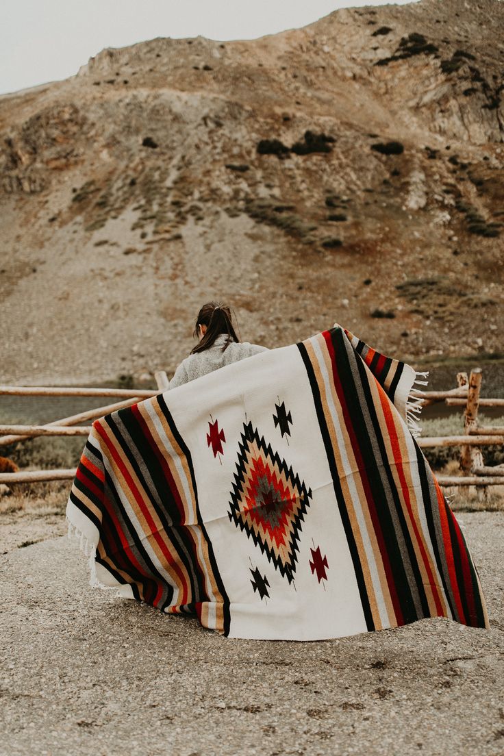 a person sitting on the ground with a blanket in front of him and a mountain behind them