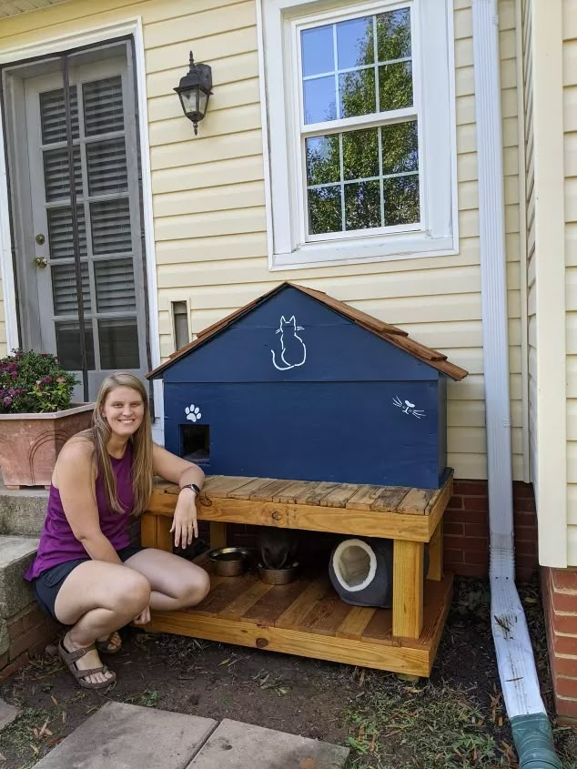 a woman kneeling down next to a dog house