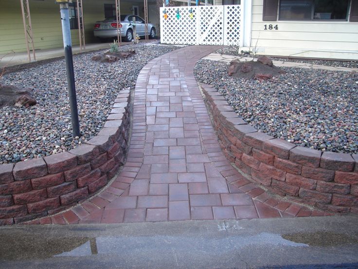 a brick path in front of a house with a car parked on the other side