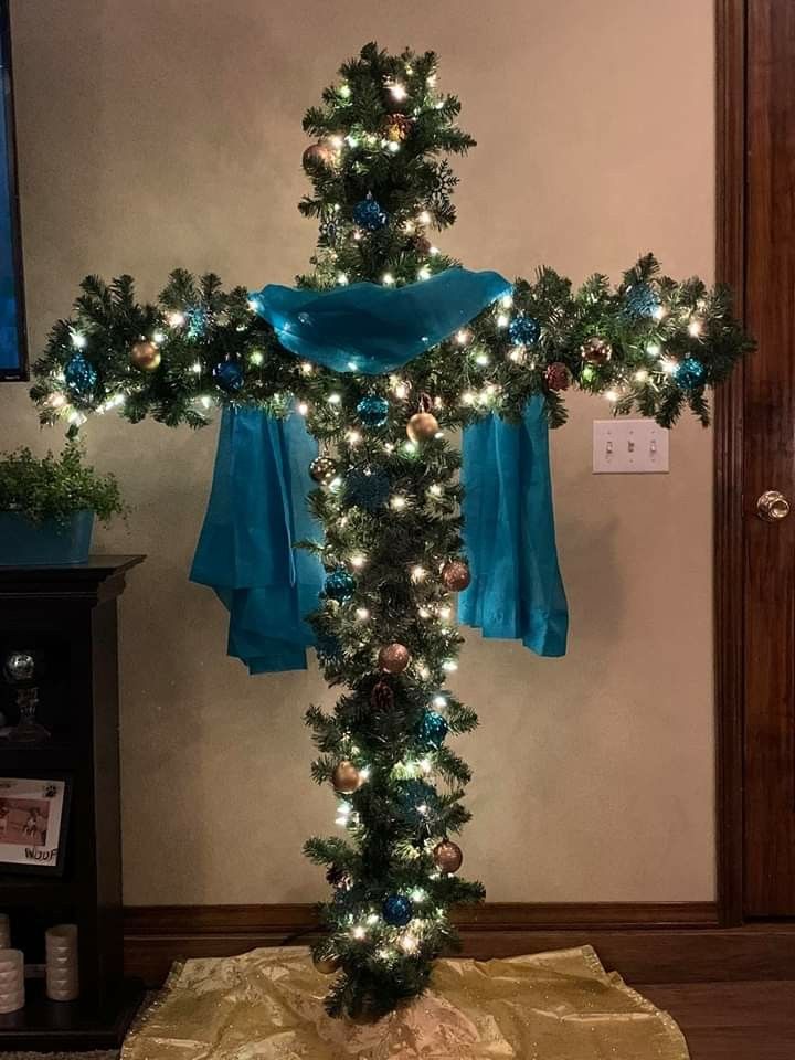 a cross decorated with christmas lights and blue ribbon is on display in the corner of a room