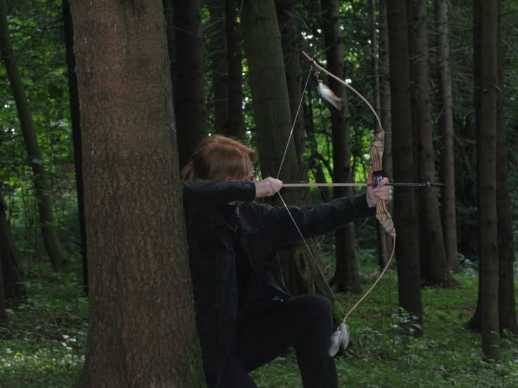 a woman aiming an arrow in the woods