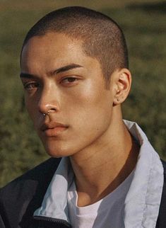 a young man is standing in the grass wearing a black jacket and white t - shirt