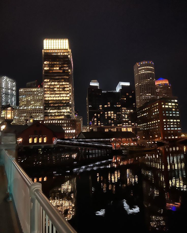 the city is lit up at night with lights reflecting in the water and skyscrapers