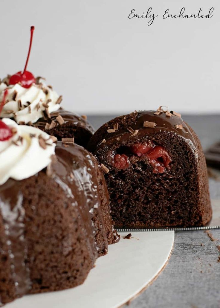 two chocolate cakes with cherries and whipped cream on top, one is cut in half