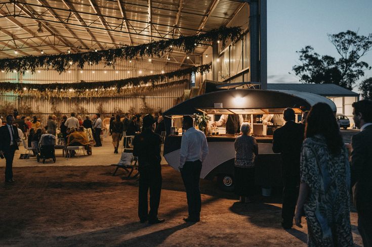 a group of people standing in front of a food truck at night with lights hanging from the roof