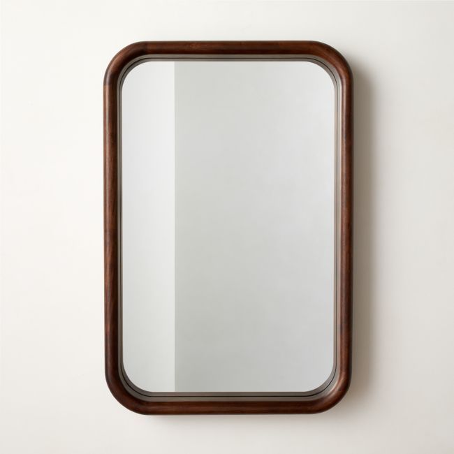 a mirror hanging on the wall next to a white wall with a brown frame and wood trim