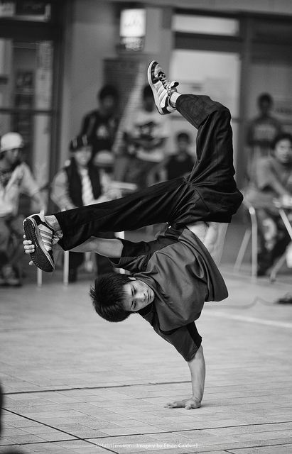 a man is doing a handstand on the ground while people watch in the background