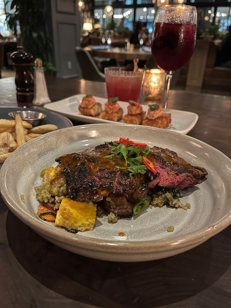 a plate with steak, rice and vegetables on it next to a glass of red wine